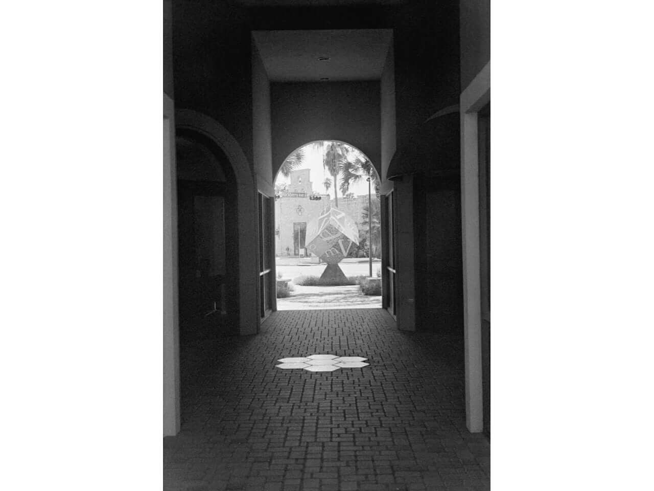 Black and white photograph of an archway leading to a geometric sculpture in courtyard, showcasing depth and contrast.