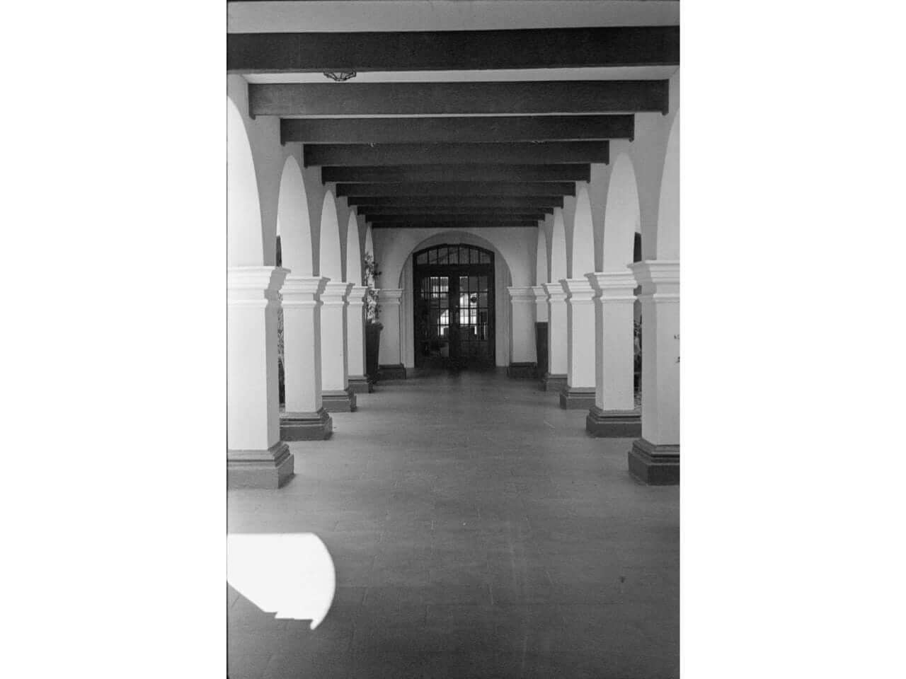 Interior hallway with arches and pillars, showcasing a monochrome aesthetic and classic architectural design.