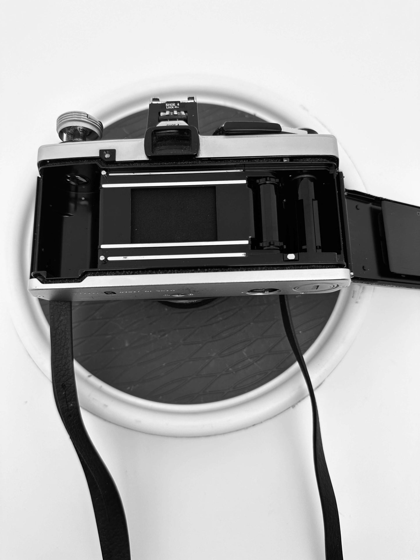 Back view of Olympus OM-2N 35mm film camera showing film compartment and strap on a circular surface.