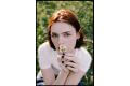 Young woman holding a flower while sitting in a field, showcasing natural beauty and soft lighting.