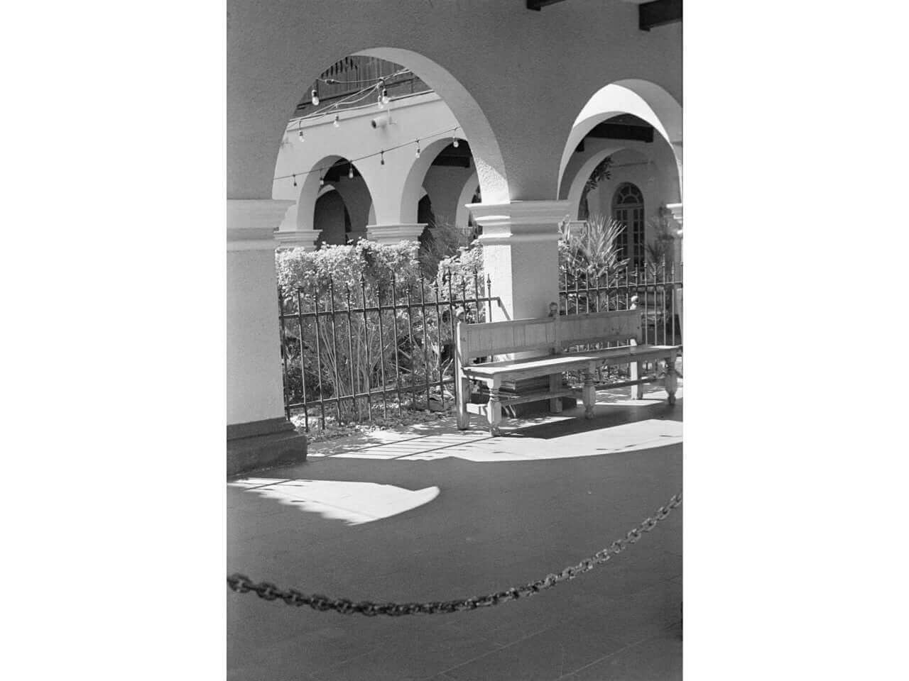 Black-and-white street scene featuring arched architecture, a bench, and shadows.