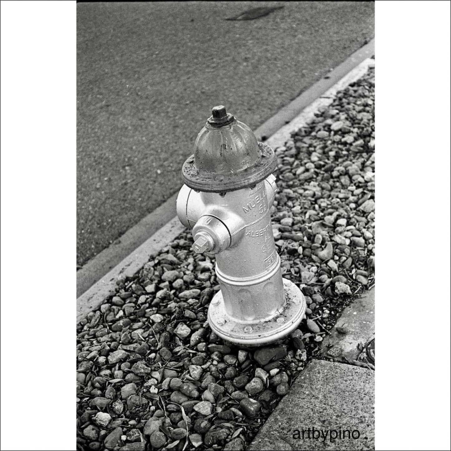 Silver fire hydrant on a rocky street edge in black and white, showcasing urban infrastructure.