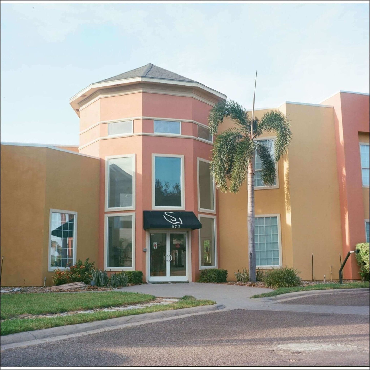 Exterior view of a colorful building with palm trees and a sign reading '501' in the entryway.