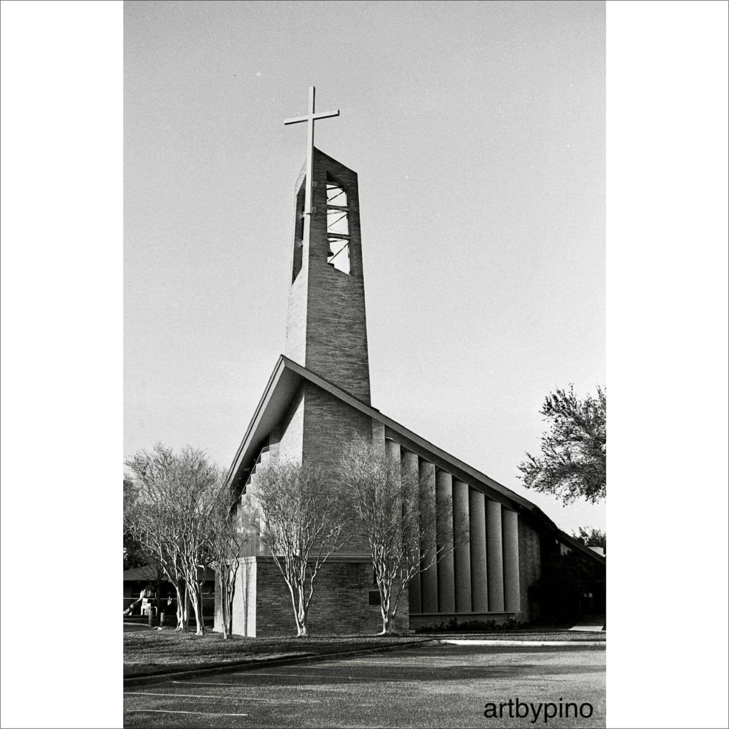 Black and white photograph of a modern church with a tall, cross-topped steeple and surrounding trees.