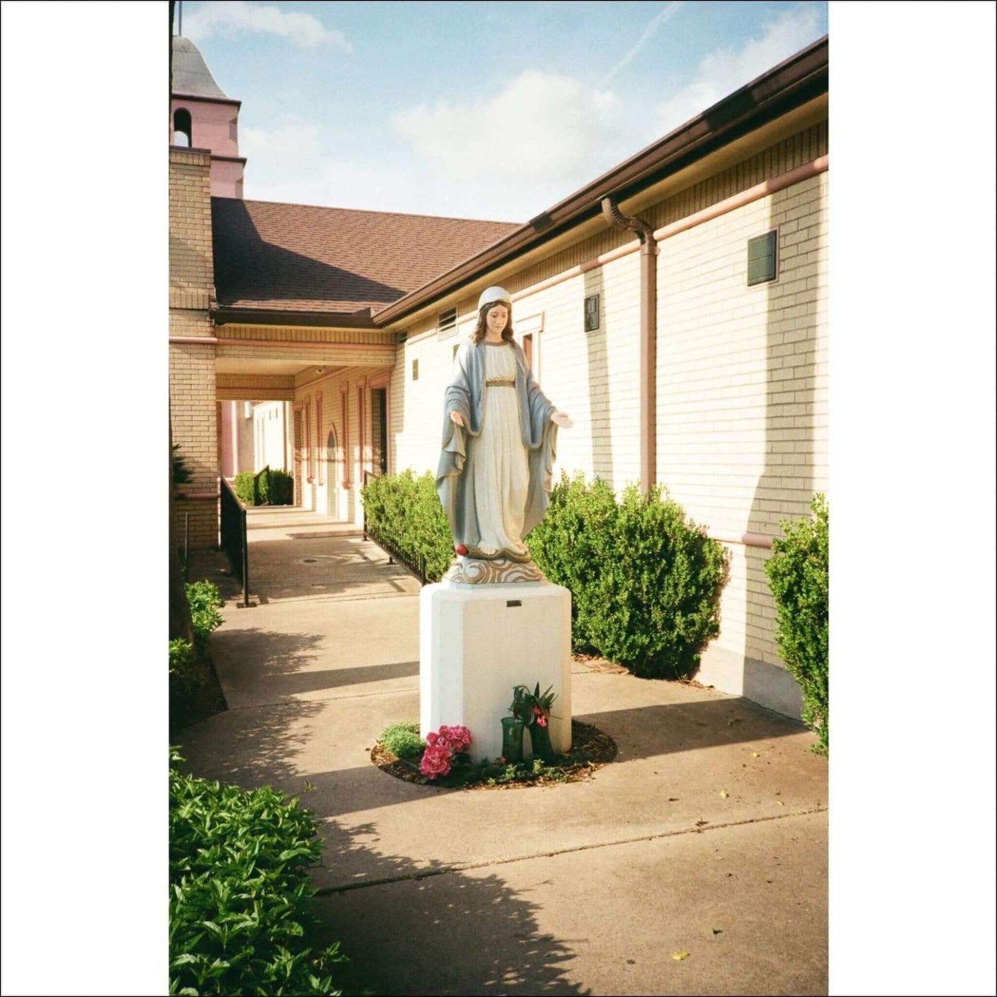 Statue of Mary surrounded by greenery at a church entrance, conveying a serene and spiritual atmosphere.