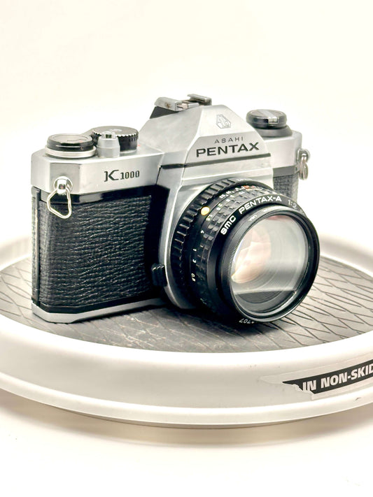 Asahi Pentax K1000 black used 35mm film camera with 50mm f2 lens on display.