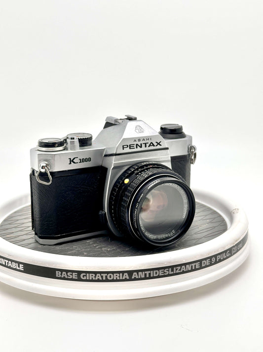 Pentax K1000 black 35mm film camera with 50mm f2 lens on a rotating display base