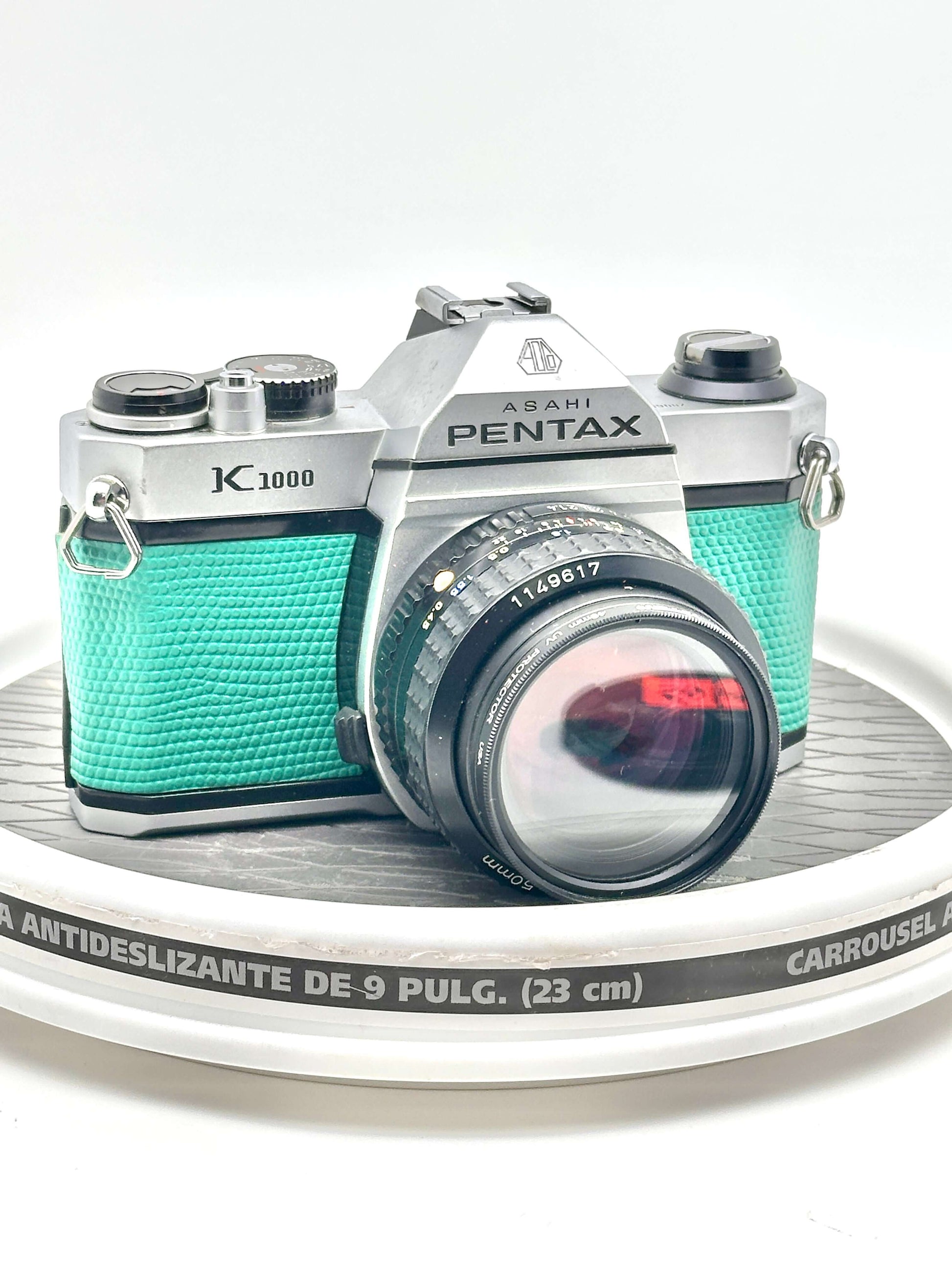 Japanese Asahi Pentax K1000 teal 35mm film camera with 50mm f1.4 lens on display.