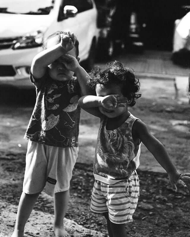 Two children playing outdoors, shielding their eyes against sunlight in a black and white photograph.