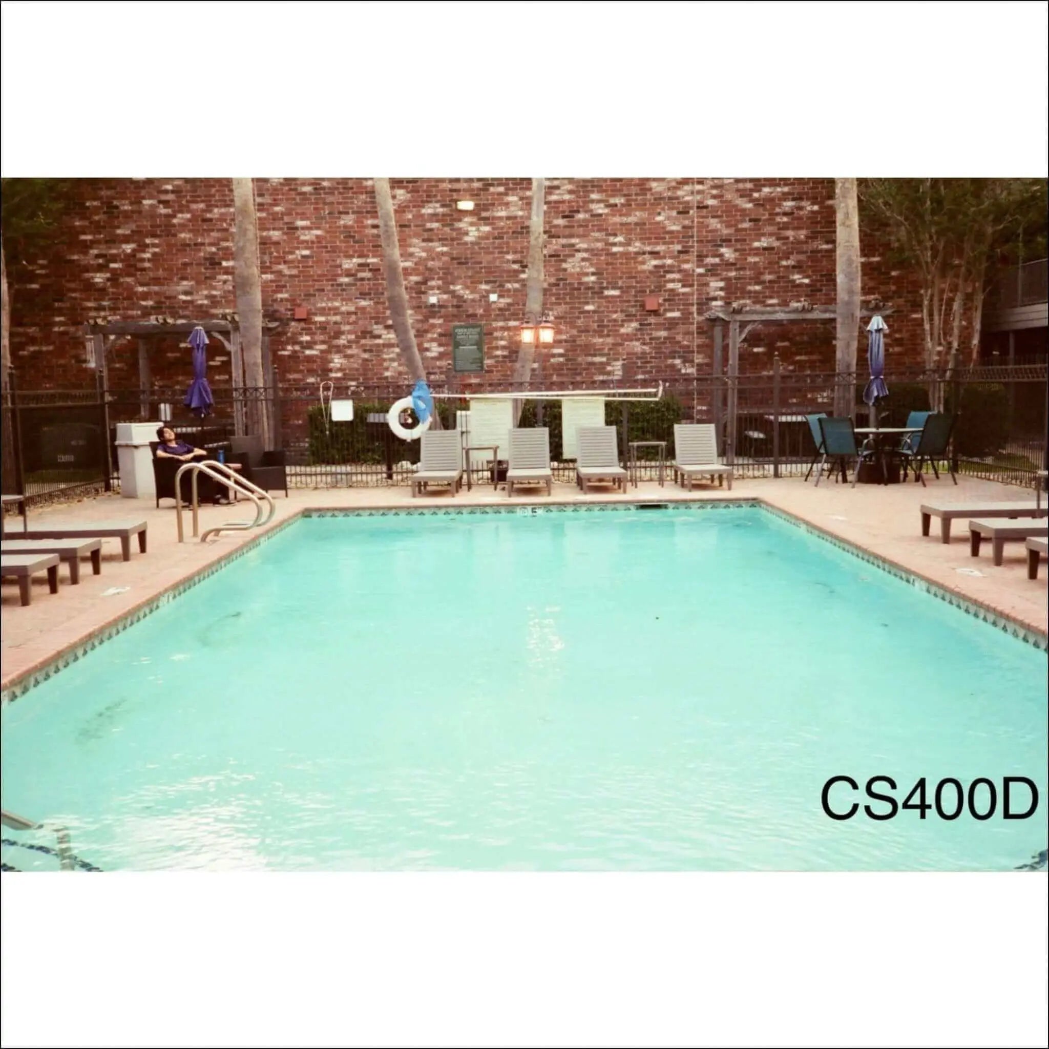 Rectangular in shape with clear turquoise water and tiled edges, surrounded by lounge chairs and a brick wall