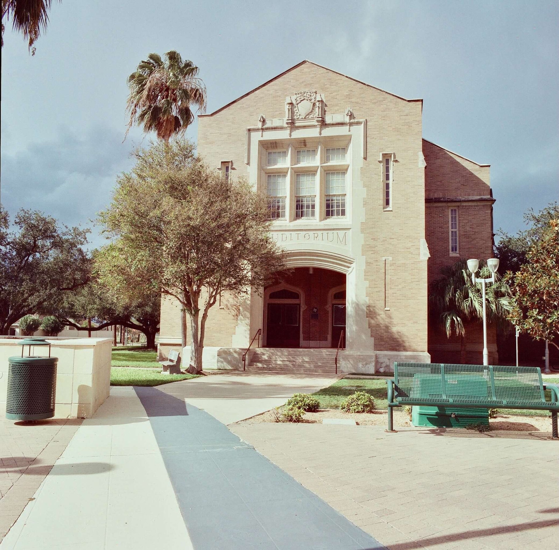 Exterior view of an auditorium building with trees and palm tree in the foreground.