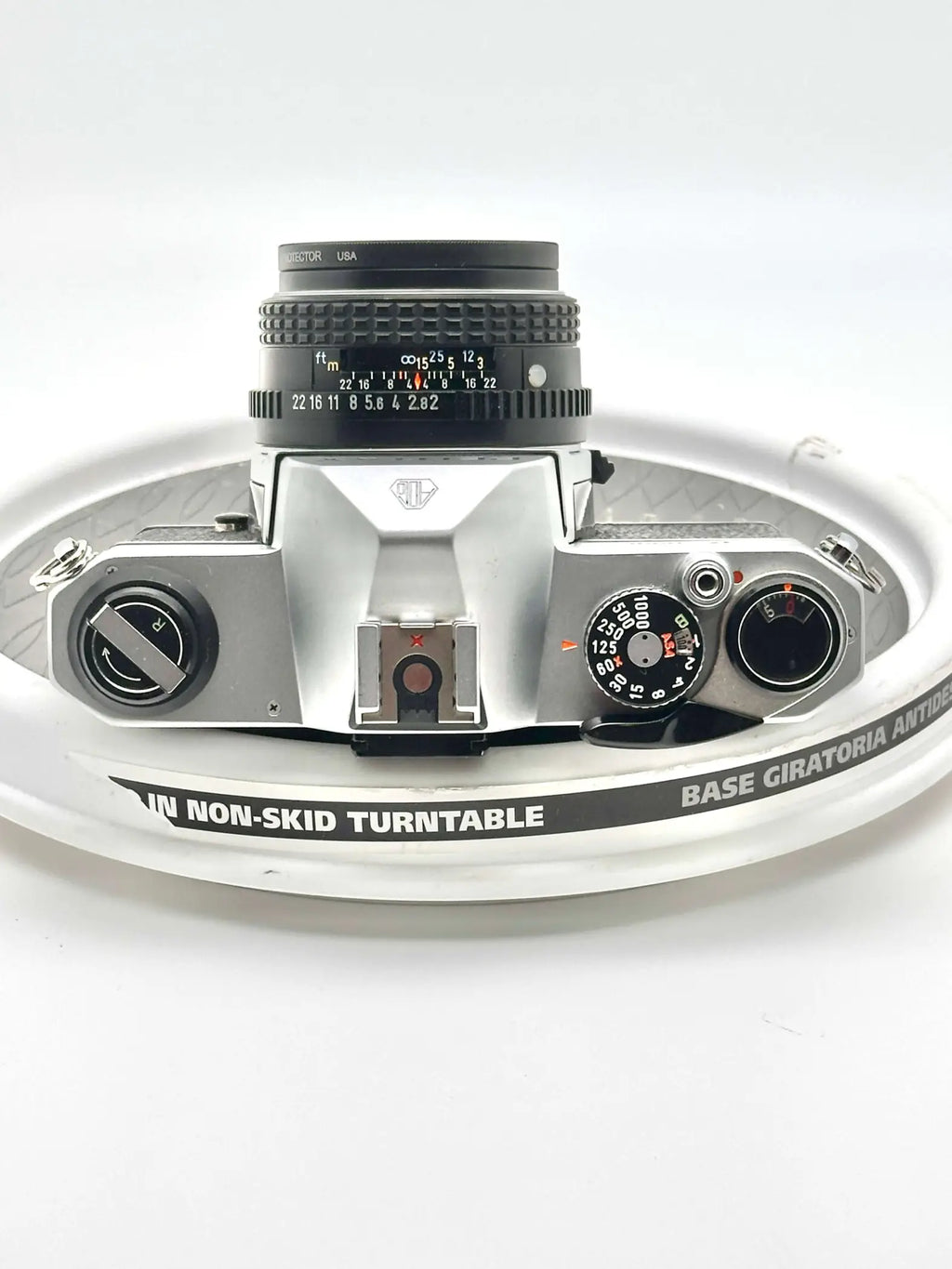 Silver-bodied canon ae-1 film camera with a black lens mounted on top, resting on a white turntable.