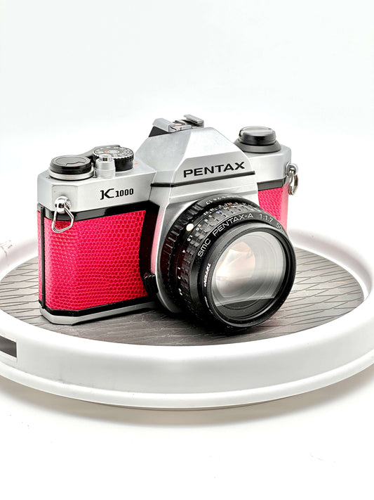 Japanese Pentax K1000 Red 35mm film camera with 50mm f1.7 lens on a rotating display.
