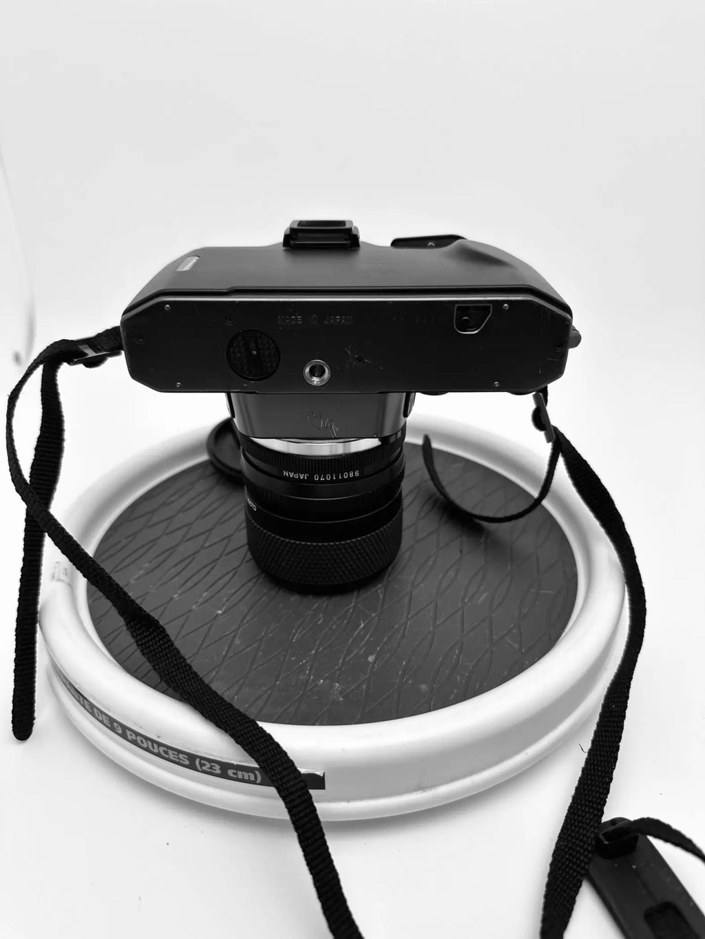Black nikon fm2 film camera with a black lens and attached strap, resting on a circular stand.
