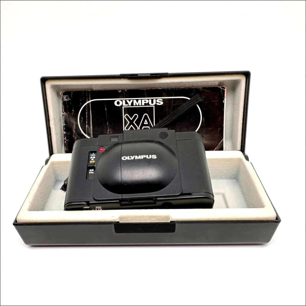 Black olympus xa compact camera with a glossy finish, nestled in its original case.