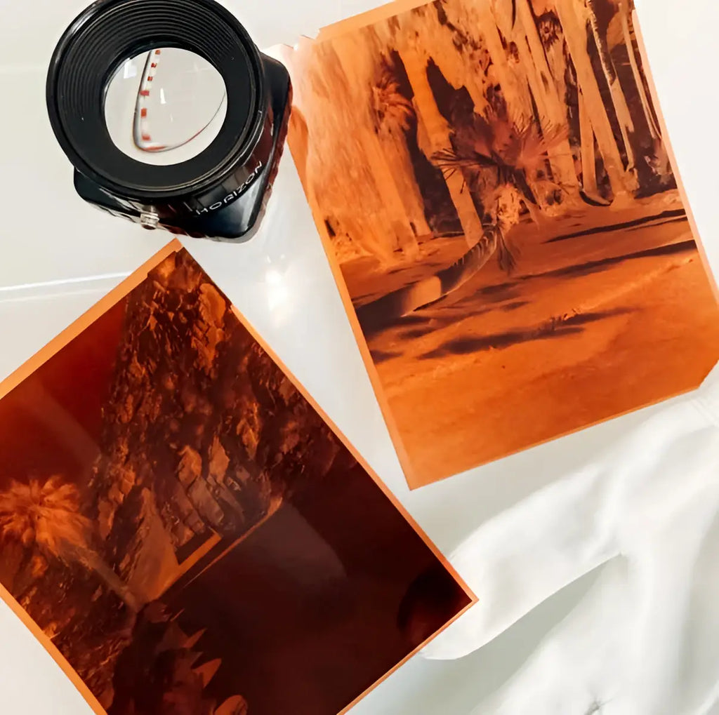 Black magnifying glass with red markings beside amber photographic prints of optik oldschool opticolour 200 c41 color negative film sheets