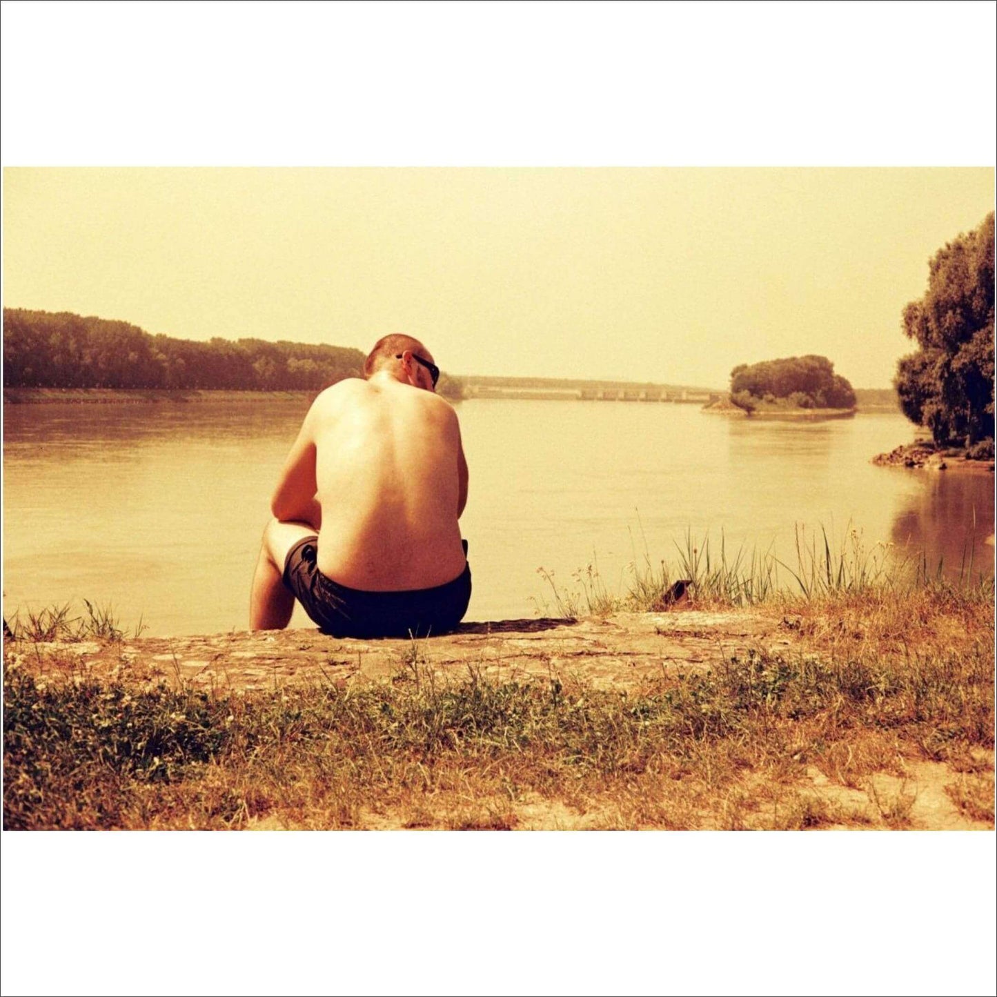 Man sitting by riverbank in warm tones, showcasing the vibrant effects of Lomography Redscale film.