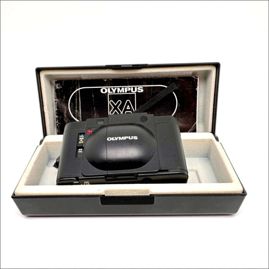 Olympus XA used 35mm vintage film camera in case with manual, showcasing its sleek design and classic features.