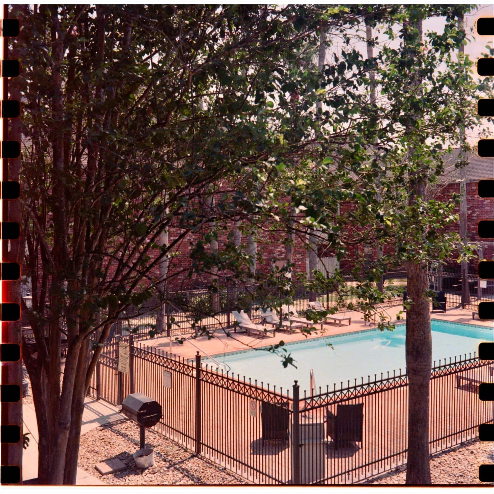 Aerial view of a swimming pool, surrounded by a fence and trees, with lounge chairs by the water.